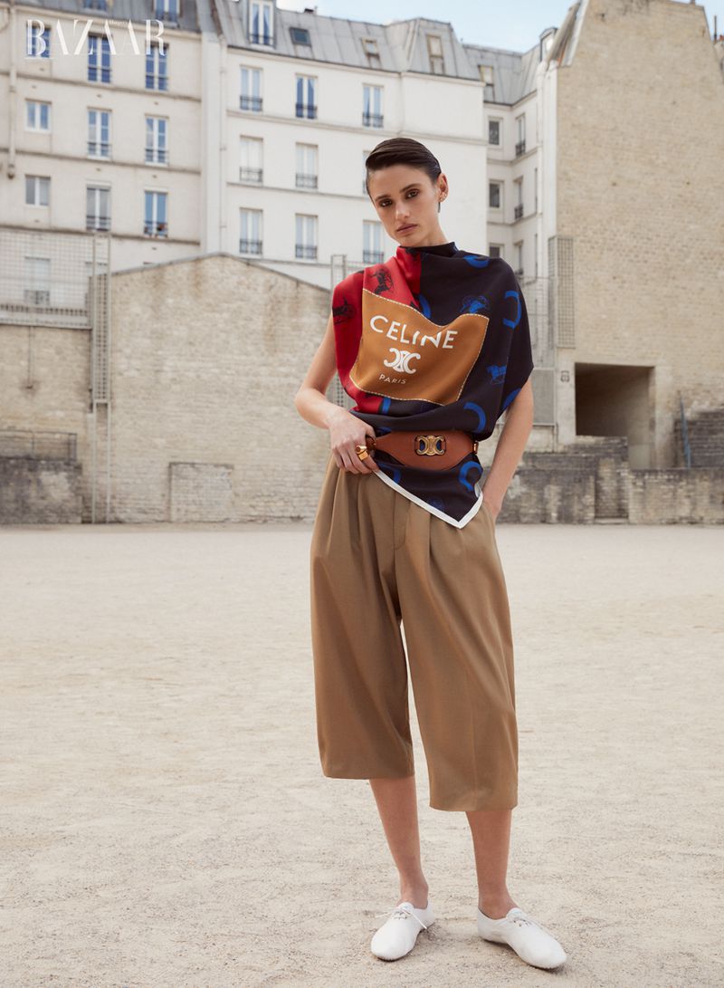 An adult female model poses in culottes and a designer scarf outdoors in an editorial fashion photograph with urban architecture.