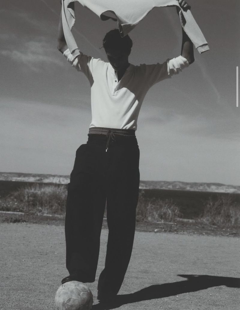 A man balances on a ball outdoors, holding a white cloth overhead. The black-and-white image features a clear sky and natural light.