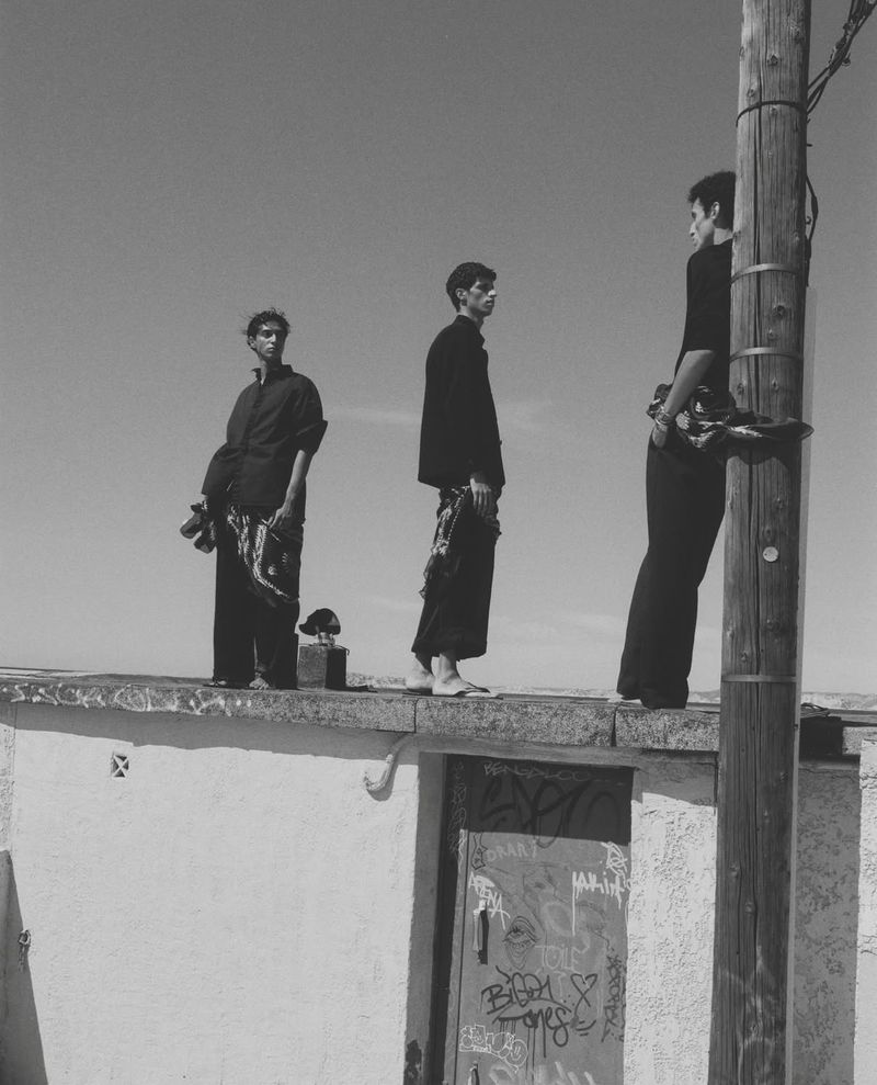 Three men stand on a rooftop near a utility pole against a bright sky. The image is black and white and has a slightly grainy texture.