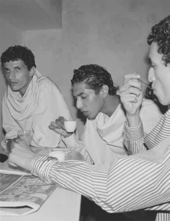 Three men seated together at a table drinking coffee and reading a newspaper in a black and white editorial shoot.