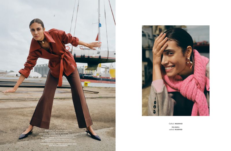 Fashion shot of a woman in a rust-colored jacket and brown pants, posing with a sailboat and dockside scene on one side and a portrait on the other.