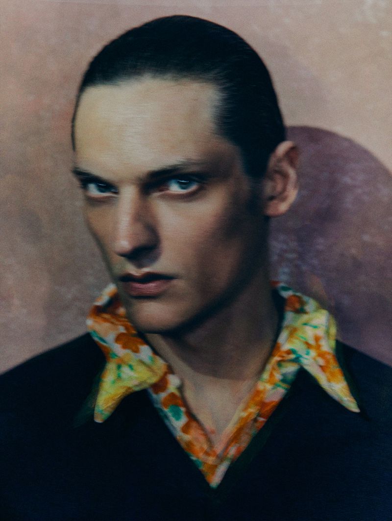 Portrait of a fair-skinned adult male with short hair, looking directly at the camera, wearing a dark shirt with a floral-patterned collar.