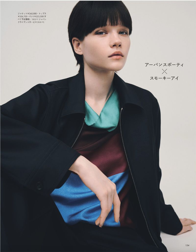 Portrait of a young woman with dark hair and a black jacket over a colourful top, in a fashion editorial studio setting.