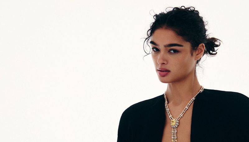 Model with dark curly hair wearing a layered diamond necklace against a bright white background for Grazia International.