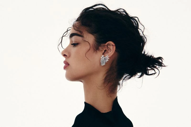 Profile shot of a woman with dark hair and a black top wearing ornamental earrings against a light background, beauty and fashion.