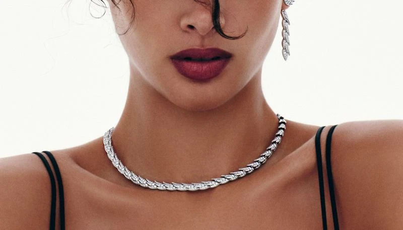 Close-up of a woman wearing a silver necklace and earrings. She has dark hair, fair skin, and red lipstick, set against a white background.
