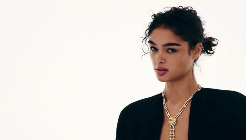 Model with dark curly hair wearing a layered diamond necklace against a bright white background for Grazia International.