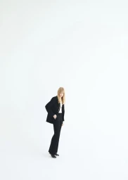 Jacqui Hooper posing in a black tailored blazer and matching trousers against an expansive white seamless backdrop for Mango Fall 2025.