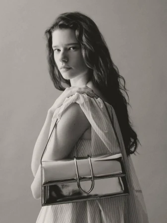 Monochrome fashion portrait of a woman with long dark hair, wearing a light dress and a shiny silver rectangular shoulder bag.