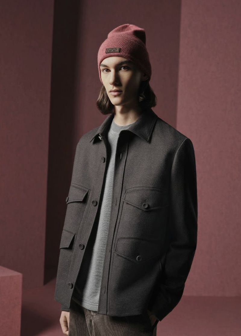 Man in stylish wool jacket and knit beanie against a monochrome backdrop. Neutral tones, indoor setting, fashion-forward aesthetic, studio lighting.