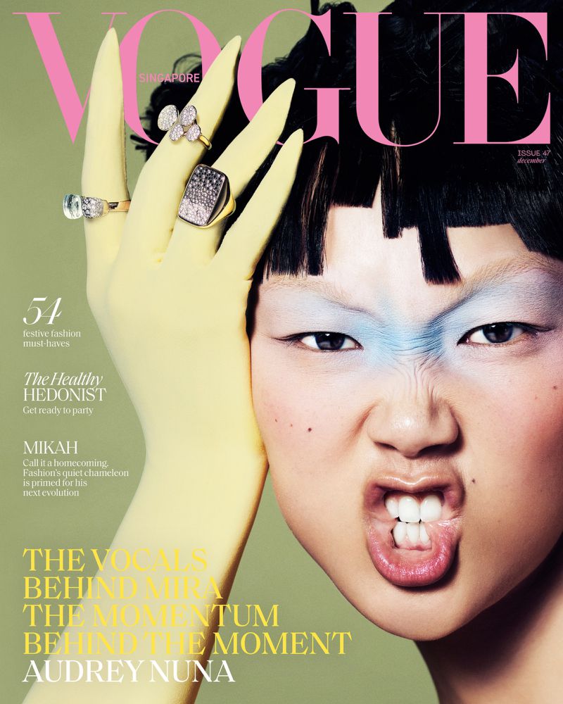 Vogue magazine cover featuring an Asian woman with bold makeup wearing yellow gloves and rings, set against a light green background.