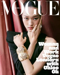 Model in black top wearing statement gold cuffs and rings against draped red fabric for Vogue Korea