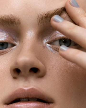 Close-up of a young adult woman's face, focusing on blue eyes, light eye shadow, and manicured fingernails on her forehead.