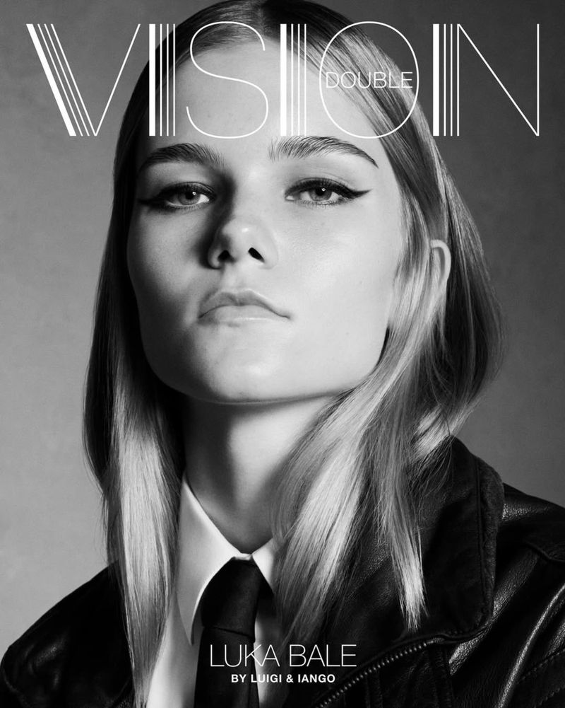 Black and white portrait of a fair-skinned adult female model with blond hair wearing a black leather jacket and tie, with graphic text.