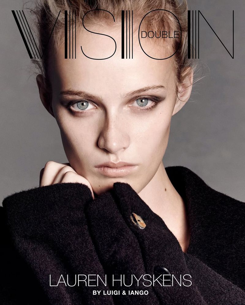 Close-up of a young woman with light skin and blue eyes, wearing a dark textured coat; fashion magazine cover art with bold typography.