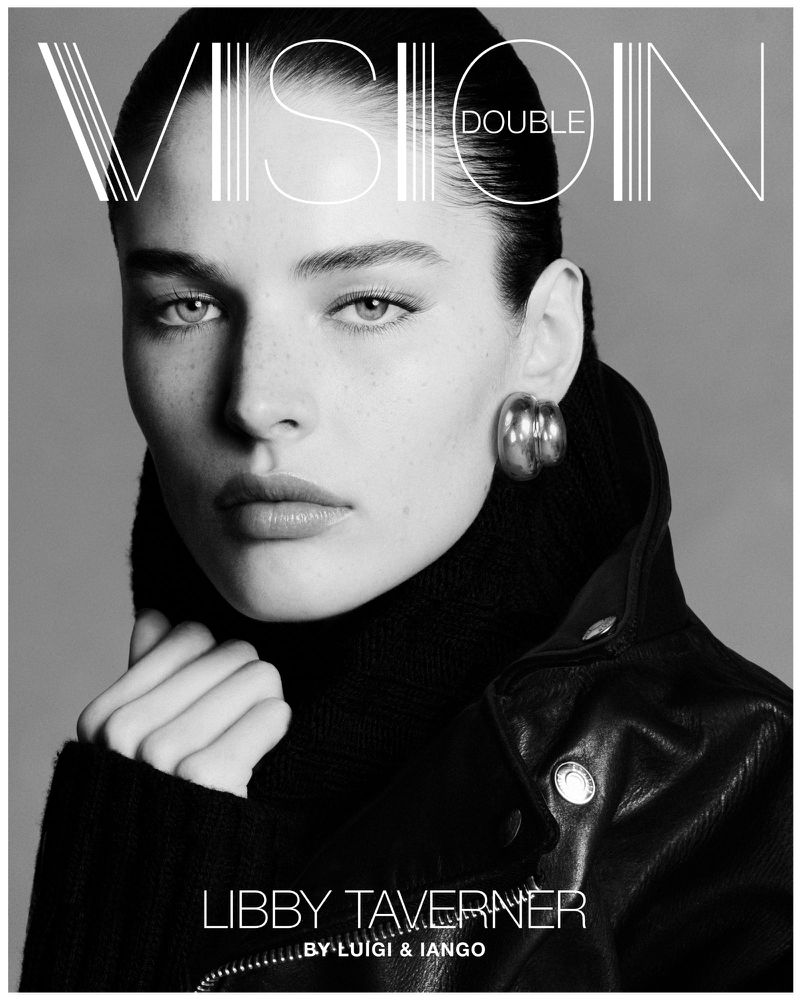 Black and white close-up portrait of Libby Taverner wearing a black turtleneck and leather jacket, gold earrings, and 'Vision Double' magazine text.