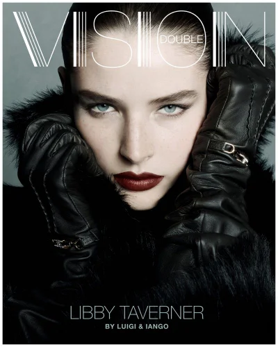 Close-up portrait of a model wearing dark leather gloves and a black coat against a grey studio backdrop.