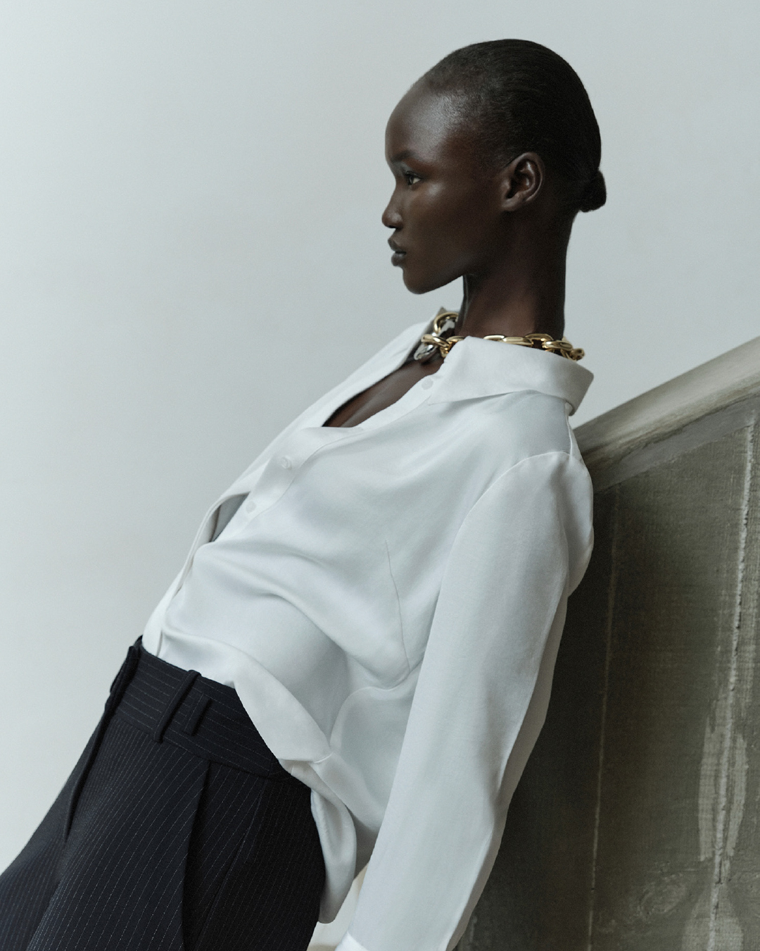 Model in a white blouse and dark trousers leaning against a textured wall for Cue SS24 campaign photographed by Pierre Toussaint
