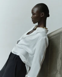 Model in a white blouse and dark trousers leaning against a textured wall for Cue SS24 campaign photographed by Pierre Toussaint