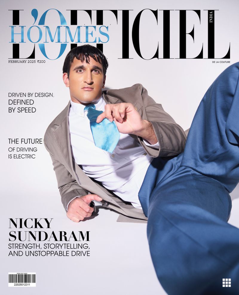 Man wearing a brown blazer, white shirt, and blue tie reclining against a plain white background for a magazine cover.