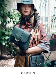 Model in green bucket hat wearing plaid top and holding dark green leather shoulder bags by Oroton for Autumn.