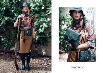 Model wearing plaid top and brown skirt holding spade outdoors with green bags