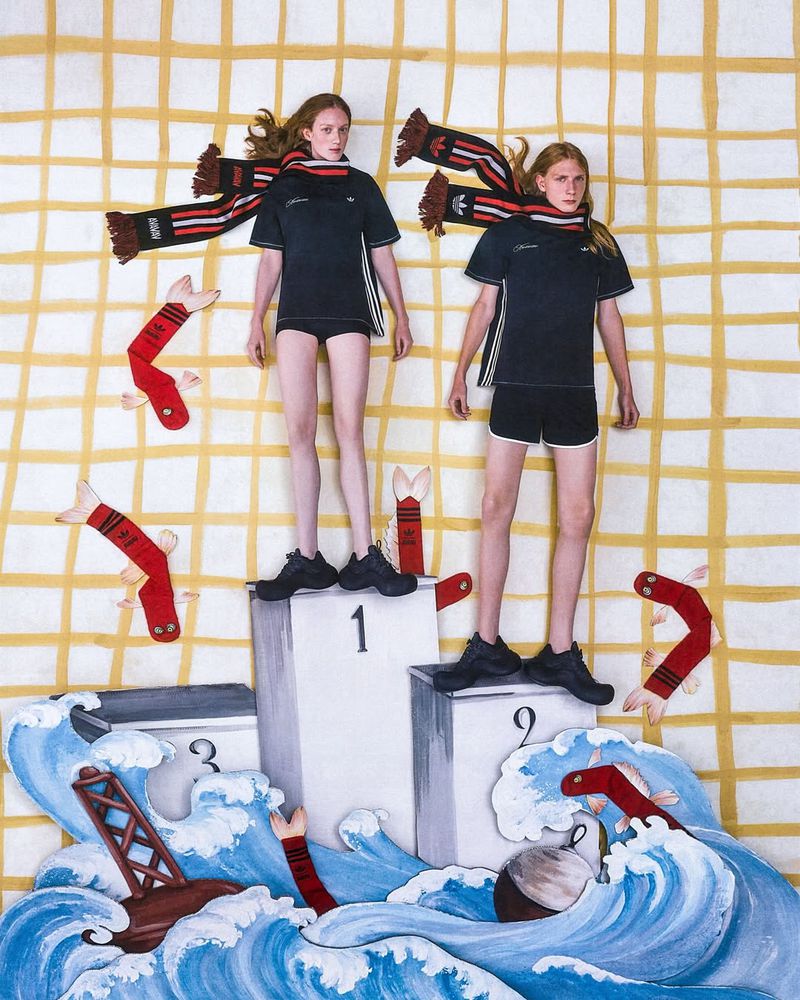Two fashion models stand on a winners' podium in a stylized editorial composition featuring illustration and a paper-cutout ocean scene.