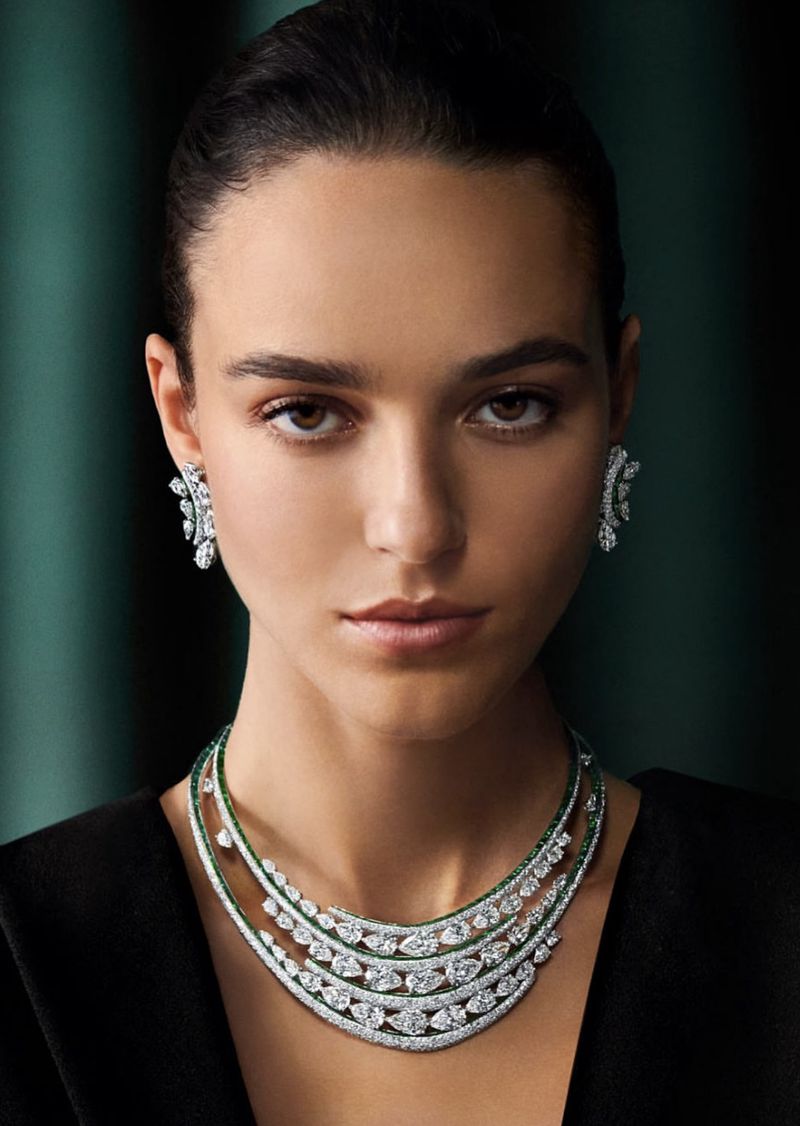 Model Emm Arruda wearing a tiered diamond necklace and matching diamond earrings against a dark green backdrop.