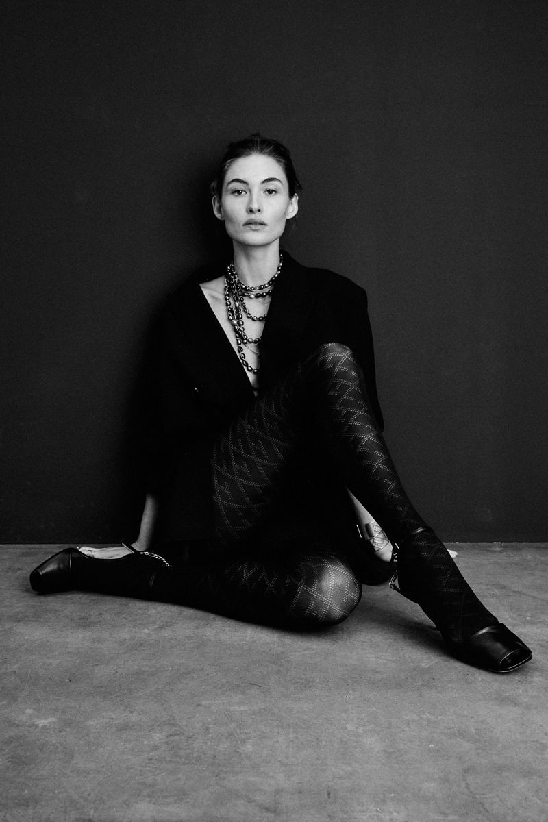 Elegant woman in patterned tights and black blazer sitting on the floor, photographed in black and white.