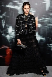 Model Grace Elizabeth wearing a black tweed jacket and long tulle skirt holding a black clutch in Bimba 2020 by Carolina Herrera