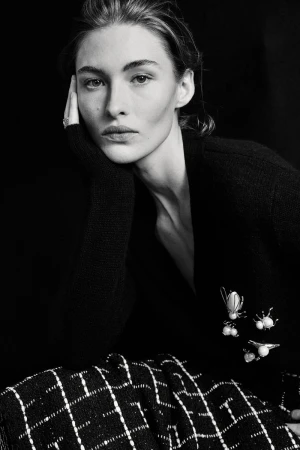 Black and white portrait of Grace Elizabeth resting her chin on her hand, wearing a black cardigan with pearl insect brooches.