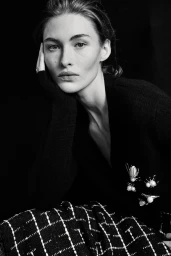 Black and white portrait of Grace Elizabeth resting her chin on her hand, wearing a black cardigan with pearl insect brooches.
