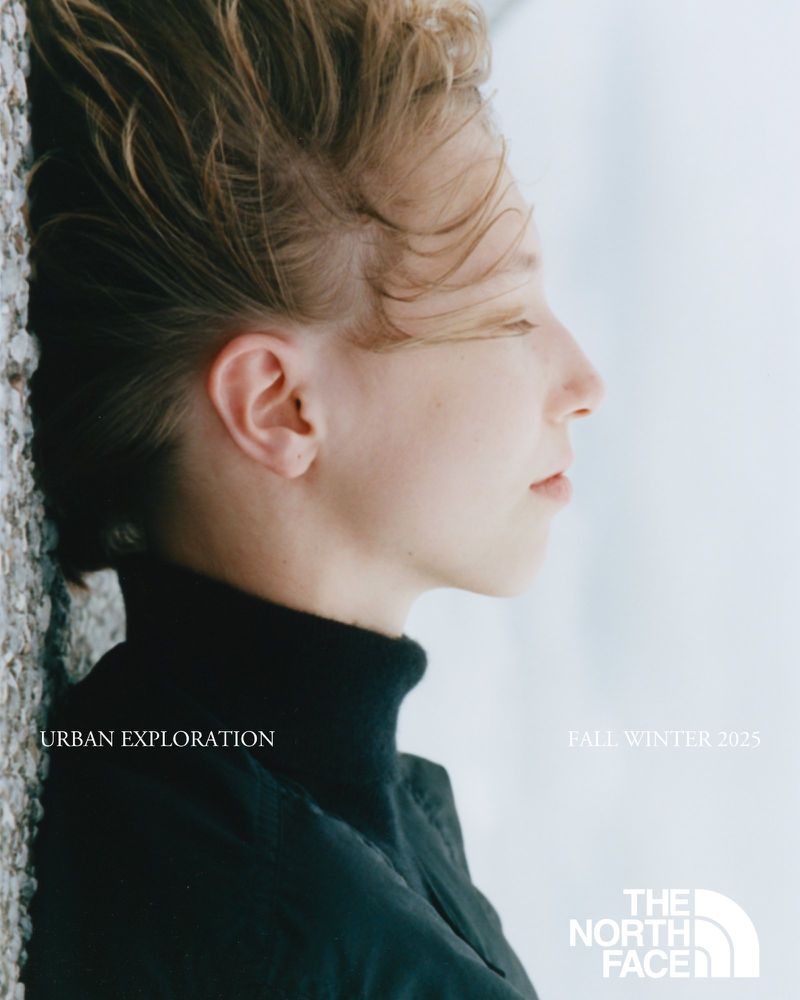 Profile view of fair-skinned person with blonde hair wearing a black turtleneck with blurred wall in soft, diffused lighting.