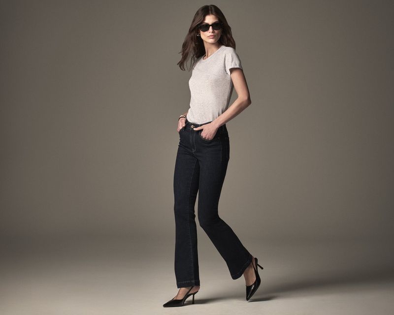 A full-length studio shot features a woman in a t-shirt, dark jeans, and heels, striking a walking pose against a neutral background.