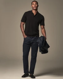 Model Niyo Malik wearing a black polo shirt and dark jeans holding a denim jacket in a studio lookbook photo for Mavi.