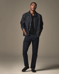 A male model posing in a dark denim jacket and matching jeans against a neutral studio background