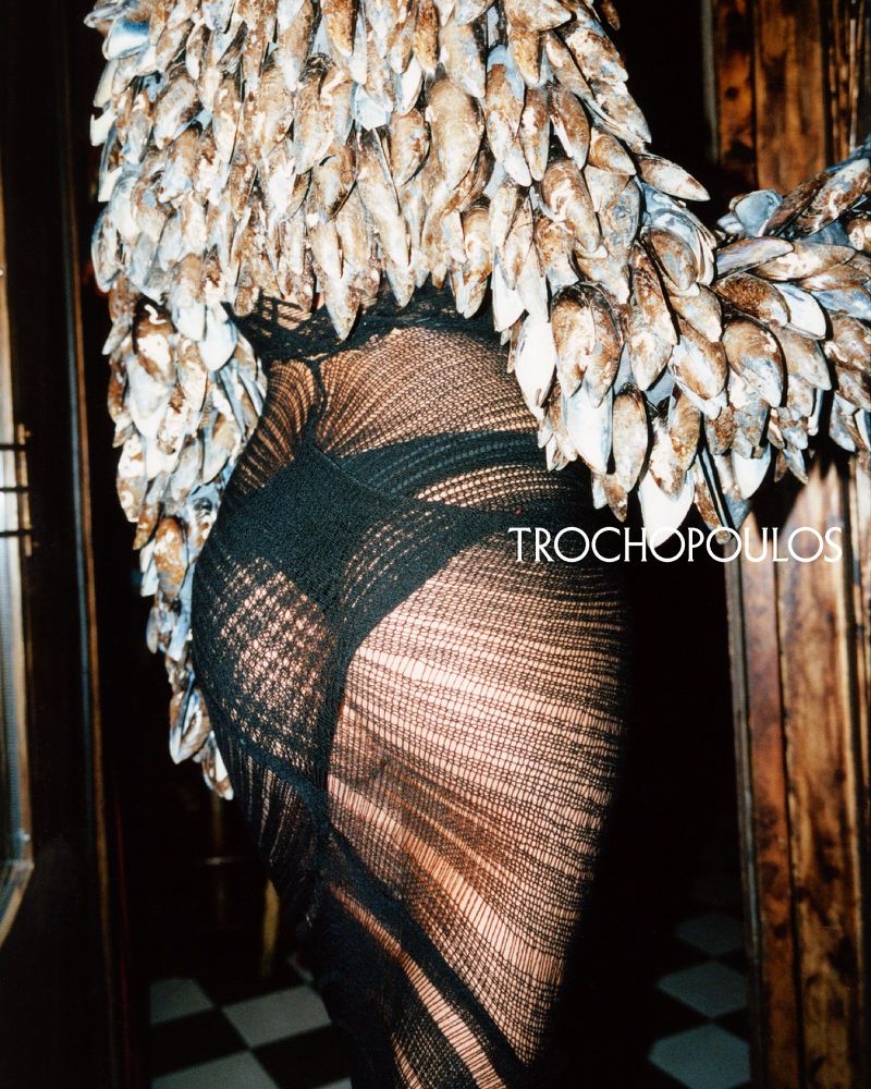 Fashionable woman wearing a black mesh dress and a sea shell top with a black and white checkered floor in the background.