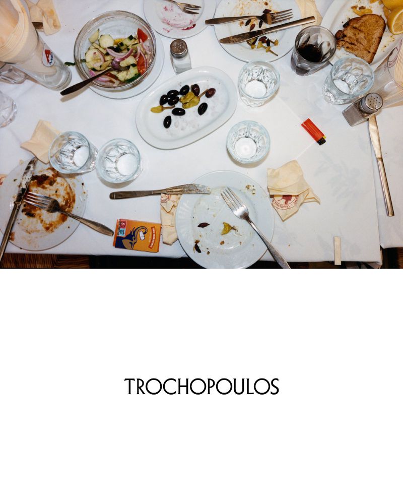 Overhead shot of dirty dinner plates, forks, knives, empty glasses, olives, and salad on a white tablecloth after a meal.
