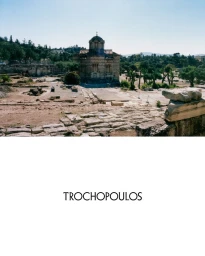 Ancient stone church and ruins landscape above centered Trochopoulos logo on white background.