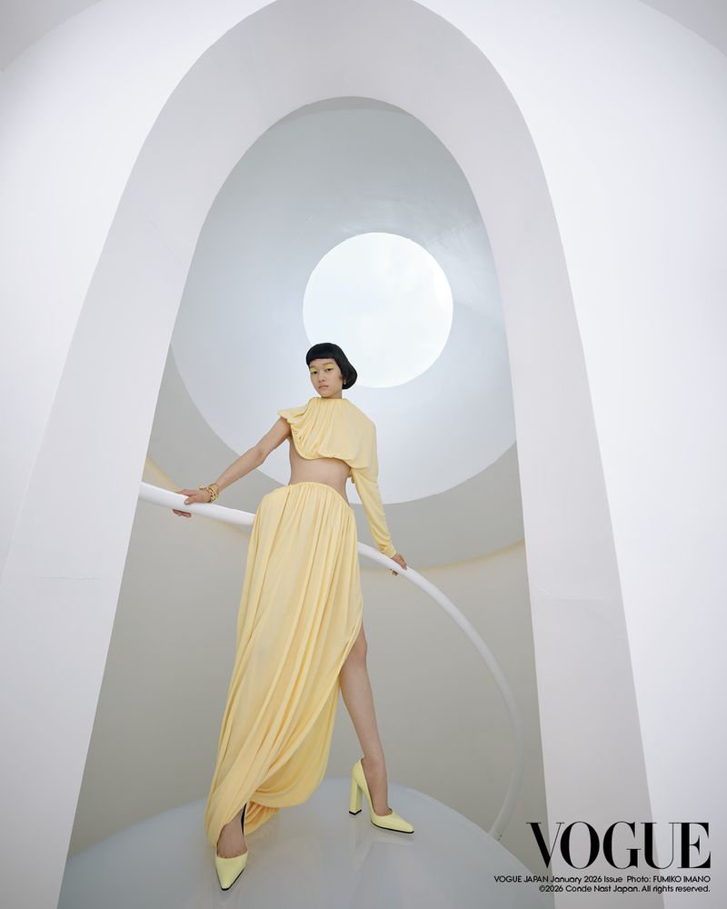 Fashion editorial shot of a woman in a yellow dress and matching high heels posing inside of an all-white modern structure.