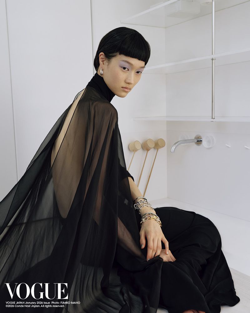 Asian woman in a black dress posing in front of white shelves and a bathroom sink with a vogue magazine logo in the corner.