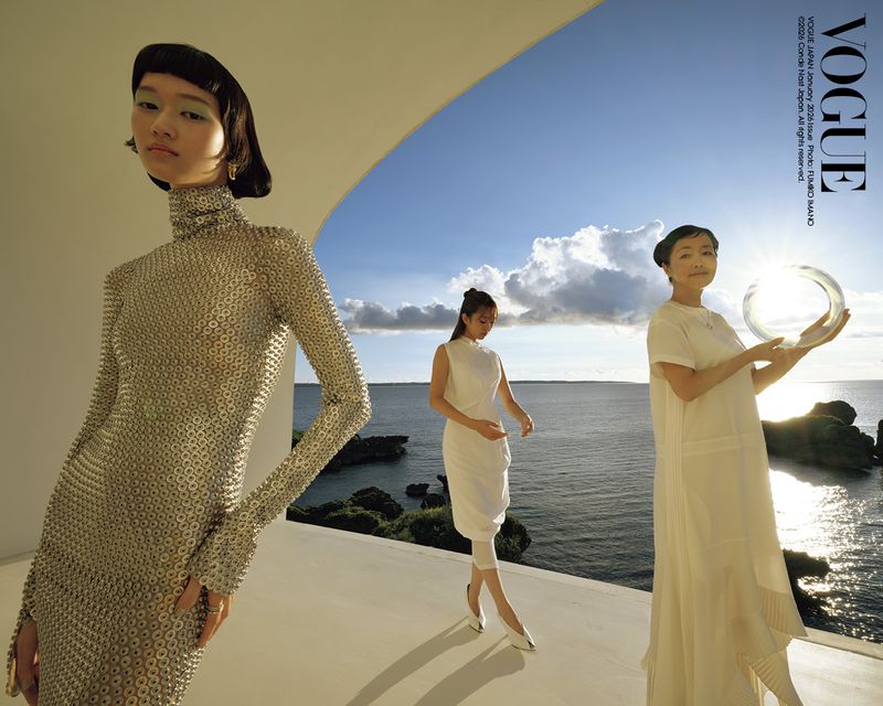 Three Asian women in white and silver dresses pose on a balcony overlooking the ocean in a Vogue Japan fashion editorial.