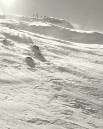 Snowy mountain landscape with wind blowing snow and a ski lift in the background, monochromatic scenery.