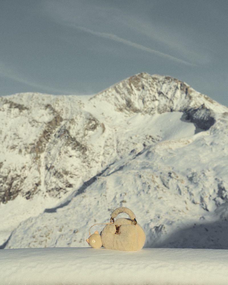 Luxury handbag displayed in a snowy mountain landscape with clear blue sky, showcasing fashion and nature with neutral color palette.