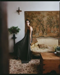 Model in long dark strapless dress seated on a vintage sofa in an interior with a large tapestry on the wall
