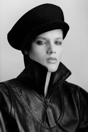 Model wearing a black cap and a dark zip-up jacket against a plain light background
