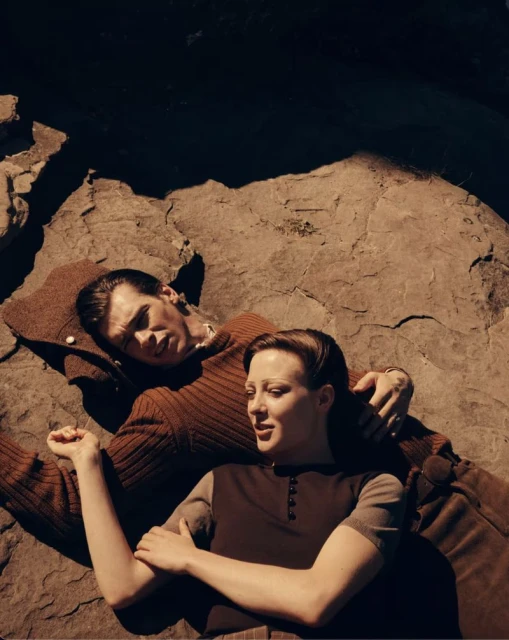 A couple lies on a textured rock surface in a medium shot. The warm-toned image showcases their casual attire and relaxed poses in natural light.