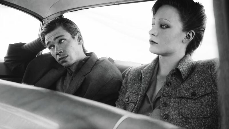 Black and white photo of a man and a woman in a car. The man is wearing a suit jacket and the woman is wearing a wool jacket.