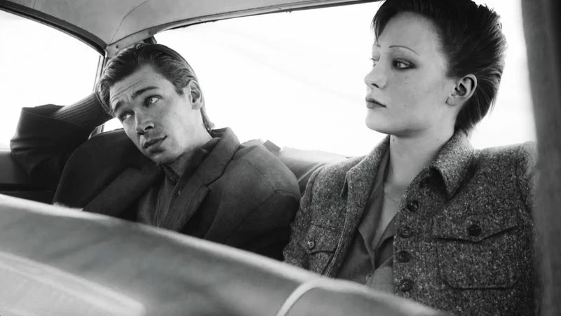 Black and white photo of a man and a woman in a car. The man is wearing a suit jacket and the woman is wearing a wool jacket.