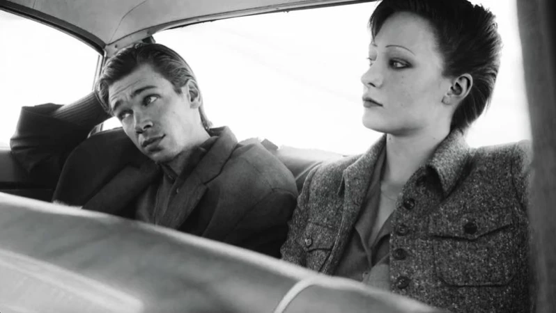 Black and white photo of a man and a woman in a car. The man is wearing a suit jacket and the woman is wearing a wool jacket.